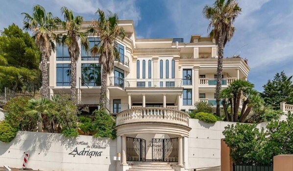 A multi-story hotel with a classical facade, palm trees, and a gated entrance.