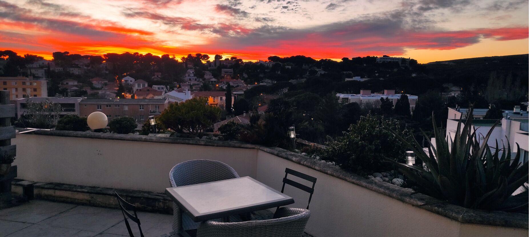 Une terrasse avec une table et des chaises donnant sur une ville au coucher du soleil.