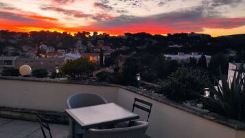 Une terrasse avec une table et des chaises donnant sur une ville au coucher du soleil.