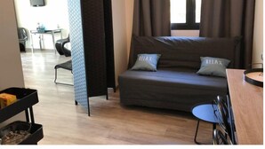 Ein modernes Hotelzimmer mit Schlafsofa, zwei Kissen mit dem Schriftzug 'RELAX', einem kleinen Tisch und einem an der Wand befestigten Fernseher.