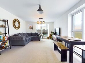 Relax in this stylish living room with a large L-shaped sofa, coffee table, bookshelf, and dining table with benches, offering a view of the city.