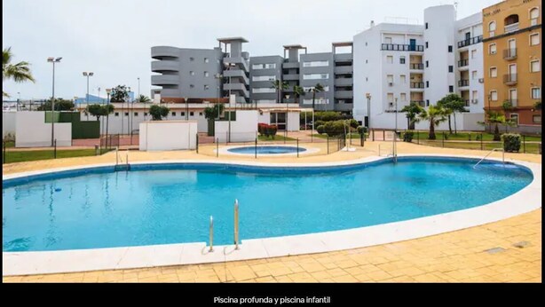 En swimmingpool med ett djupt område och en separat barnpool, omgiven av moderna byggnader.