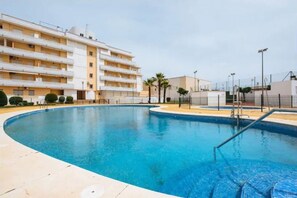 Ein Pool mit geschwungener Kante, umgeben von einer niedrigen Mauer und einem Gebäude mit mehreren Balkonen.