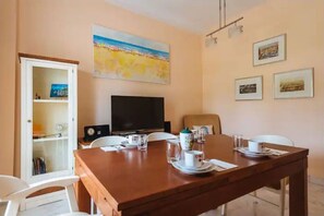 A dining area with a wooden table, chairs, a television, and a painting of a beach scene on the wall.