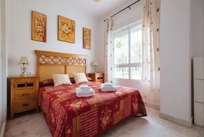 Ein ordentlich eingerichtetes Schlafzimmer mit einem großen Bett, zwei Nachttischen und einem Fenster mit Vorhängen.