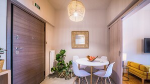 Una habitación de hotel moderna con una puerta de madera, una mesa redonda de comedor con sillas, una planta en maceta, un televisor montado en la pared y un sofá amarillo.