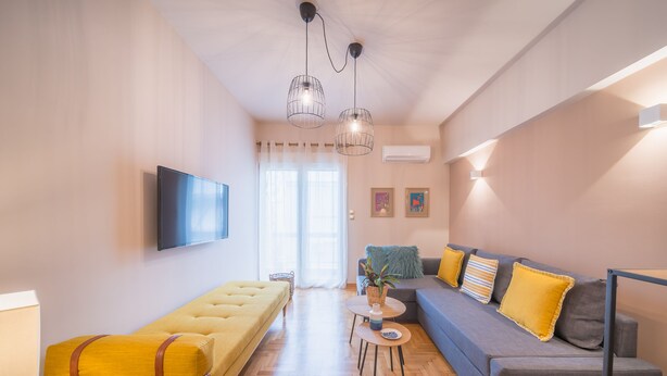 Una sala de estar moderna con un sofá, un sillón amarillo, un televisor montado en la pared y una mesita con una planta.