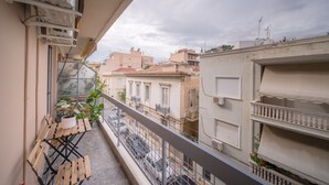 Un balcón con muebles de madera, plantas en macetas y vistas de edificios cercanos.