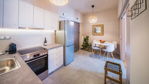 Una cocina moderna con electrodomésticos de acero inoxidable, una zona de comedor con sillas blancas y un taburete de madera.