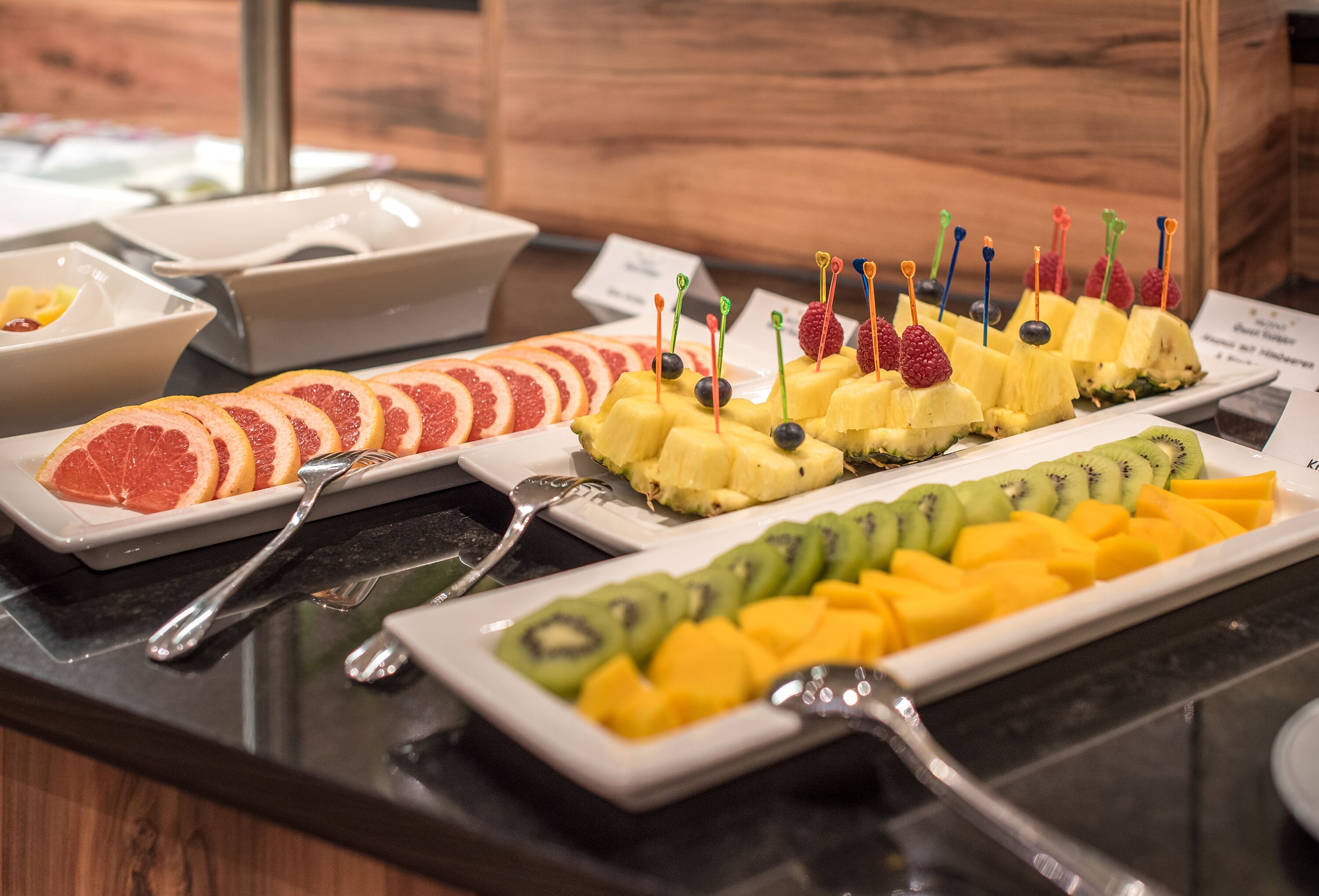 A buffet with various fruit platters, including grapefruit, pineapple, kiwi, and mango.