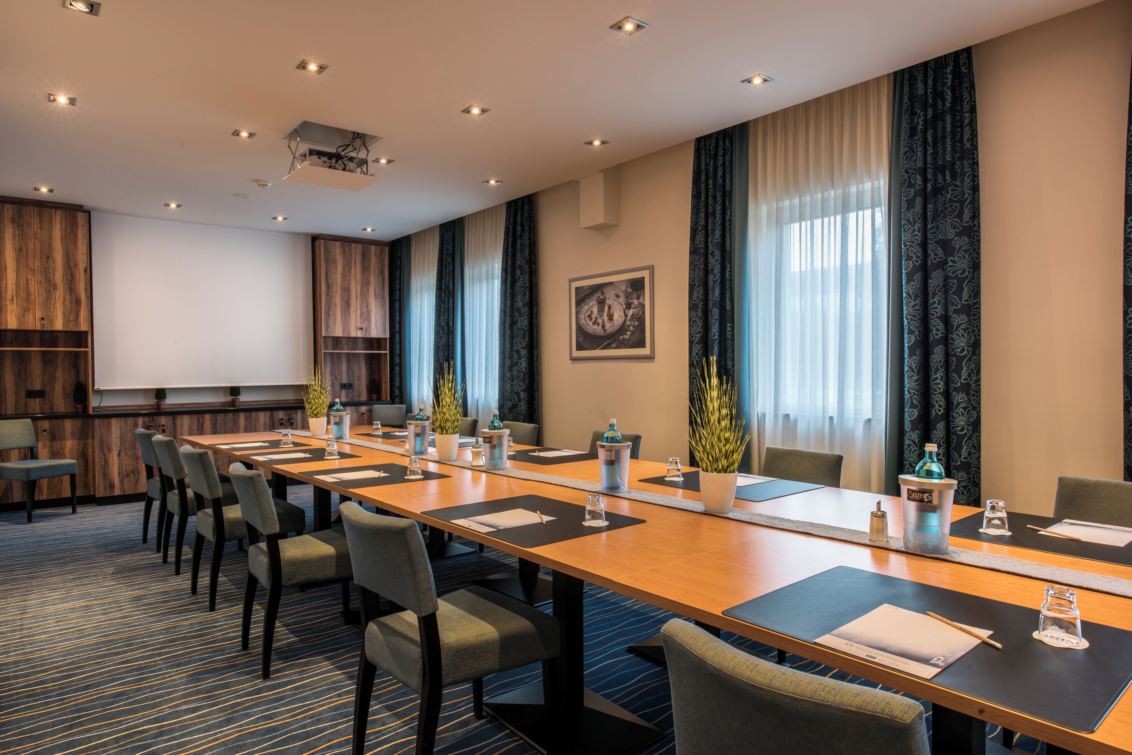 A conference room with a long table, chairs, a projector, and a large window with curtains.