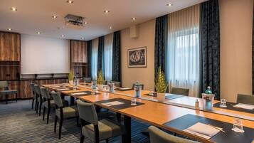 Ein Konferenzraum mit langem Tisch, Stühlen, einem Projektor und einem großen Fenster mit Vorhängen.