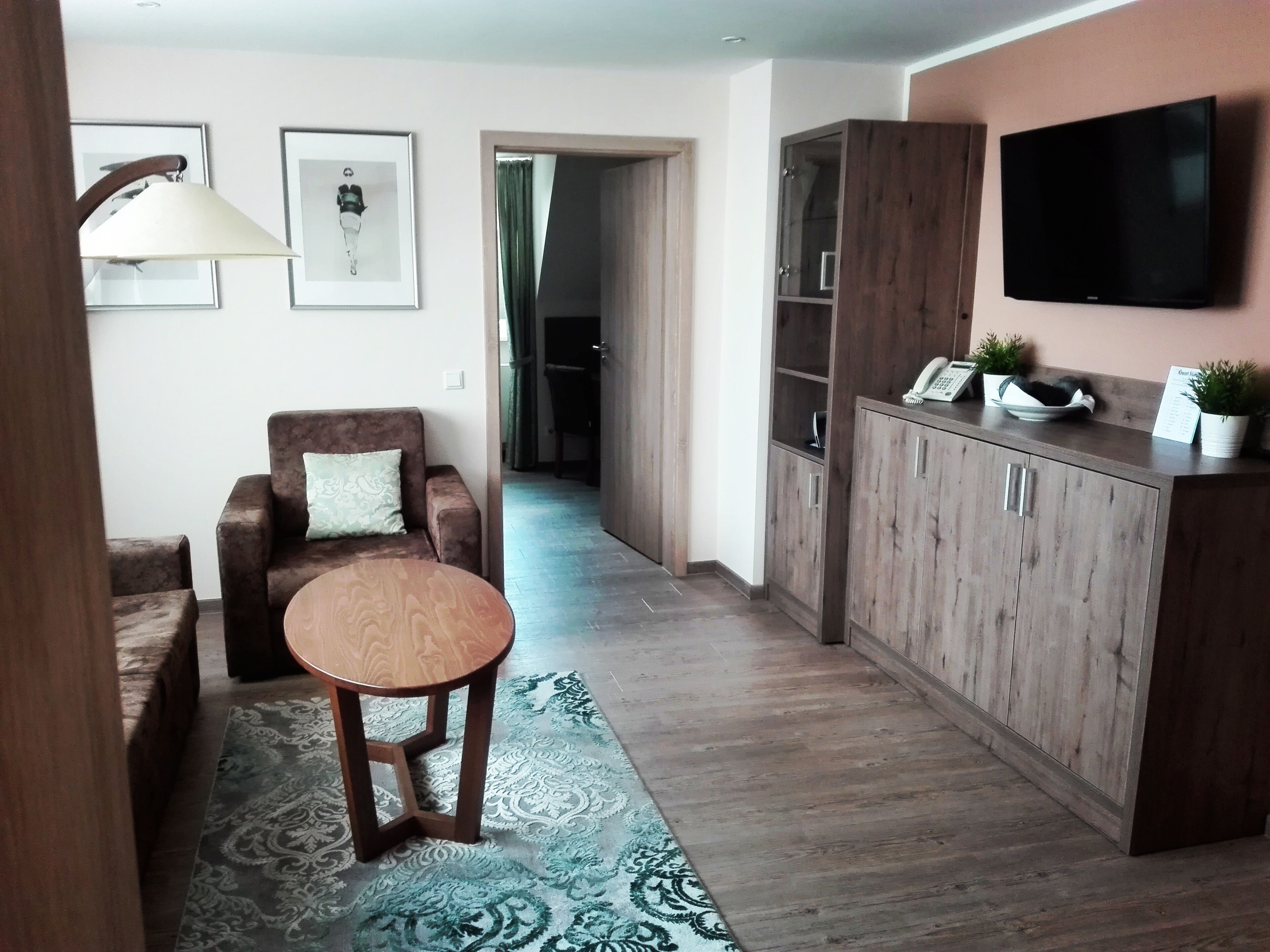 Un salón con sofá, una mesa redonda de madera, un armario y un televisor de pantalla plana montado en la pared.
