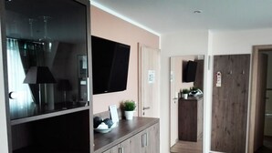 A modern interior with a flat-screen TV, wooden cabinets, a potted plant, and a kitchen area with a wooden door. - Akzent Hotel Köhler (Giessen)