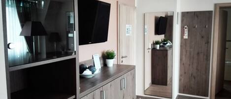 A modern interior with a flat-screen TV, wooden cabinets, a potted plant, and a kitchen area with a wooden door.