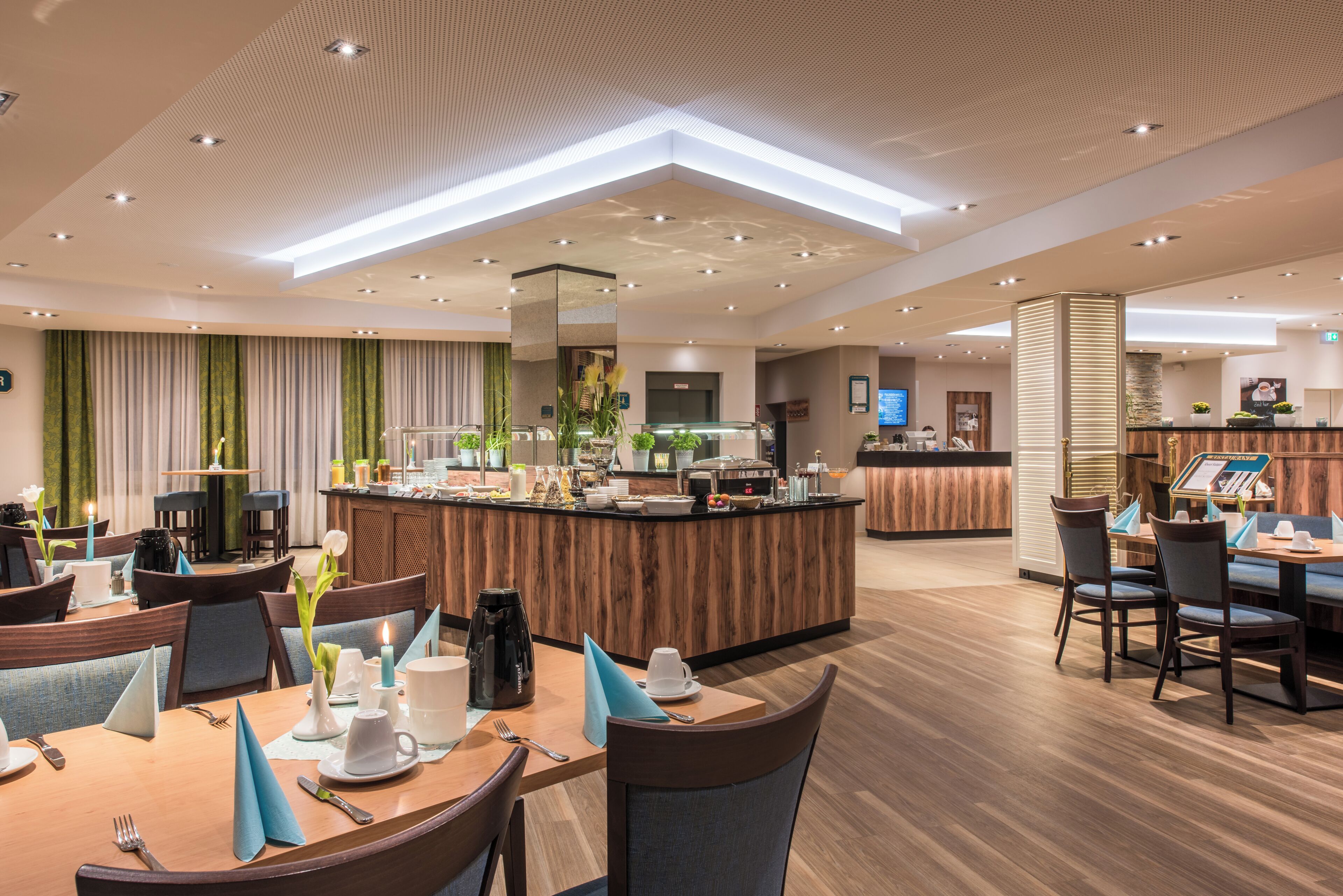 A modern hotel lobby with a central bar, dining area, and a reception desk.