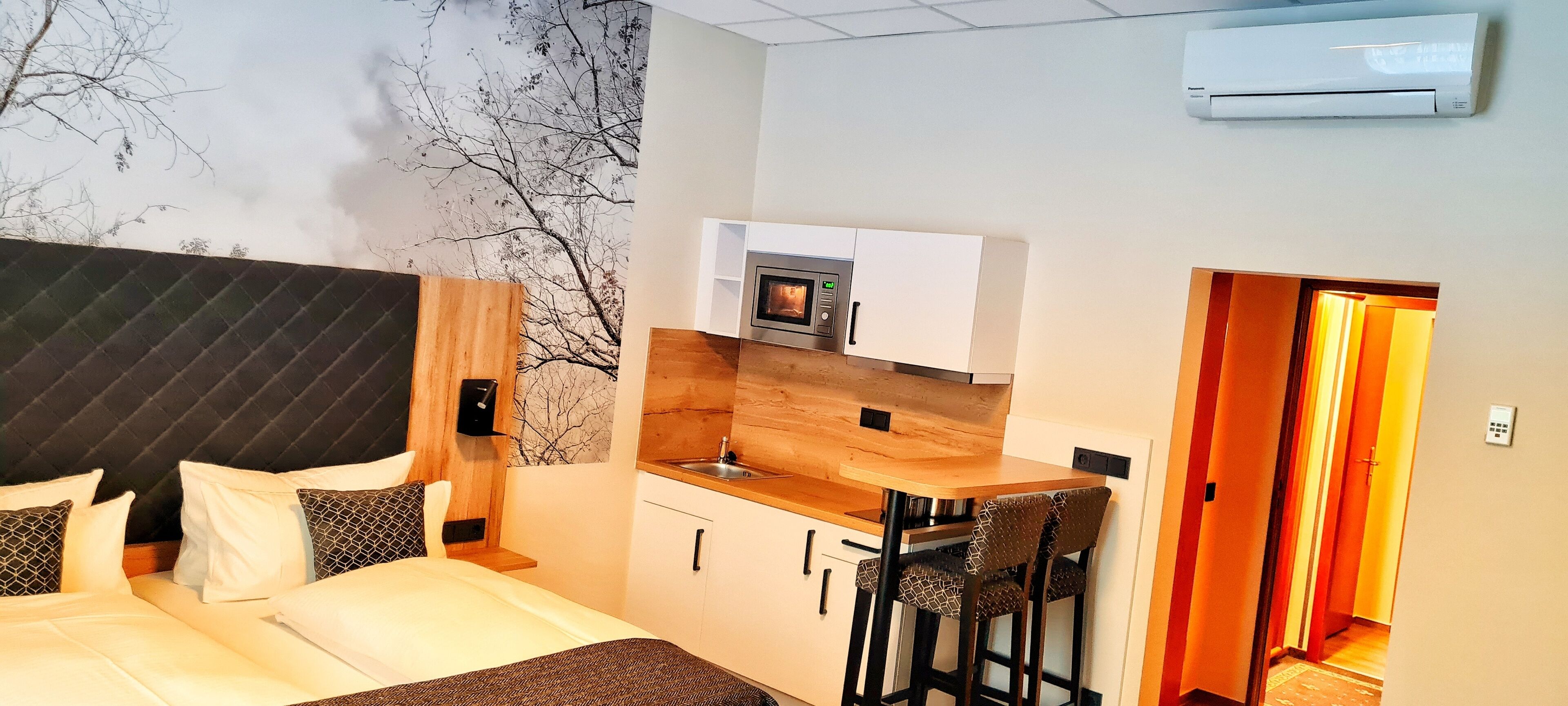 Habitación de hotel compacta con cama, una kitchenette pequeña y un comedor con dos sillas.