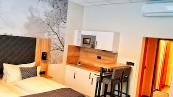 Habitación de hotel compacta con cama, una kitchenette pequeña y un comedor con dos sillas.
