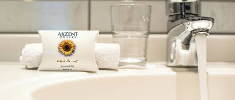 Un lavamanos de baño con una toalla, un vaso de agua y un paquete con la etiqueta 'AKZENT Hotels - Klassic für Sichei'.