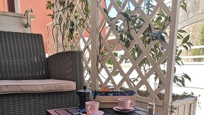 Un patio con un sofá de mimbre, una mesa de madera con tazas rosas y un fondo de celosía.