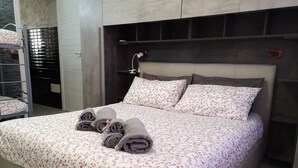 Un dormitorio moderno con una cama grande, cabecera con iluminación integrada y una litera a la izquierda.