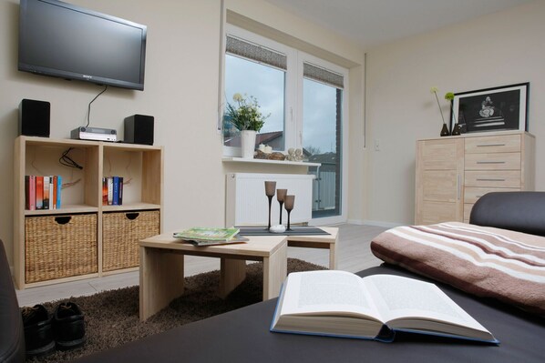 Quarto moderno com televisão de tela plana, escrivaninha de madeira, estante, janela com vista, cama e cómoda.