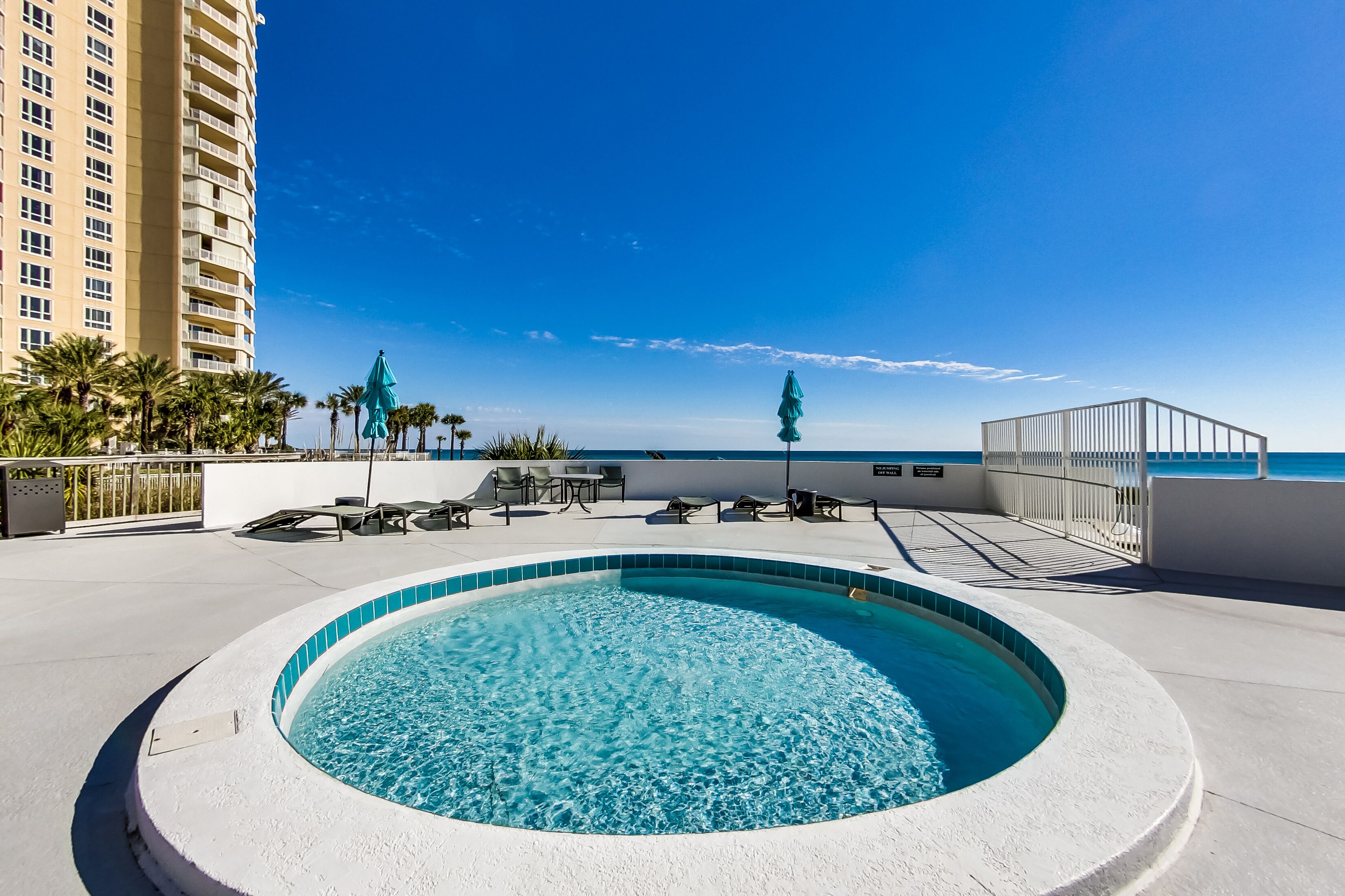 Piscina no terraço com vista ampla para o oceano, rodeada por espreguiçadeiras e um edifício alto.