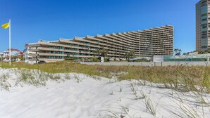 A large, multi-story hotel with a modern architectural design, located near a beach with sand dunes. - Edgewater 409 - Gulf Views! Beach & Pool Access! (Miramar Beach)