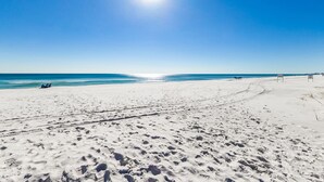 A beach with footprints leading to the water, a clear sky, and a few people in the distance. - Edgewater 409 - Gulf Views! Beach & Pool Access! (Miramar Beach)