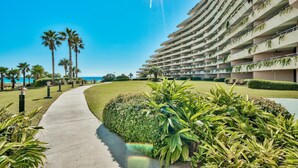 A modern hotel with a curved facade, a landscaped pathway, and palm trees. - Edgewater 409 - Gulf Views! Beach & Pool Access! (Miramar Beach)