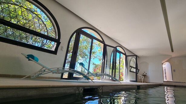 Ein Innenpool mit großen Glaswänden, eine Lounge mit einem Sessel und Blick auf viel Grün.