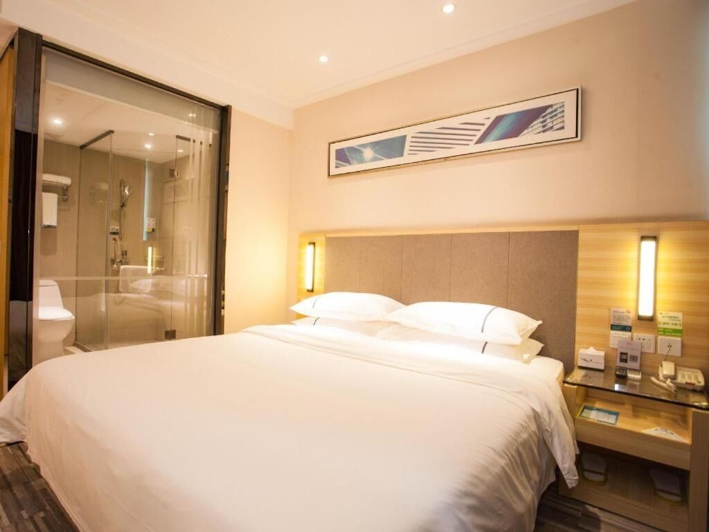 A hotel room with a large bed, a glass shower enclosure, a wooden headboard, and a framed artwork on the wall.