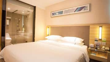 A hotel room with a large bed, a glass shower enclosure, a wooden headboard, and a framed artwork on the wall.