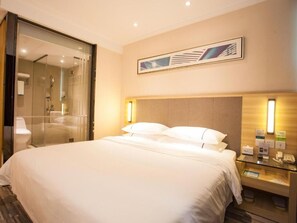 Un cuarto de hotel con una cama grande, cabina de ducha de vidrio, un cabecero de madera y una obra de arte enmarcada en la pared.