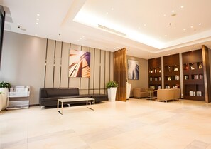 A modern lobby with a sofa, coffee table, bookshelves, and a potted plant. - City Comfort Inn (Zhanjiang)