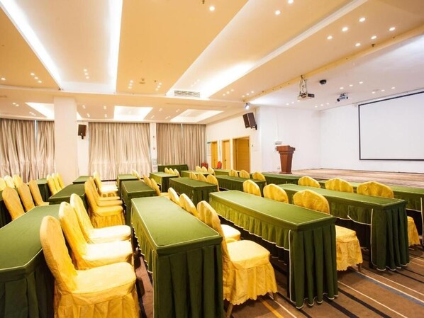Une salle de conférence avec des rangées de tables et de chaises, un pupitre et un écran de projection.