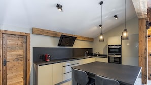 Une cuisine moderne dotée d’un îlot central, d’appareils électroménagers intégrés et de luminaires suspendus.