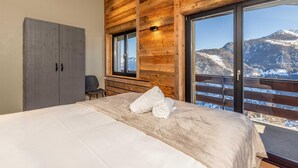 Une chambre avec un grand lit, des murs en bois, une vue sur les montagnes et un balcon doté d’une balustrade en bois.