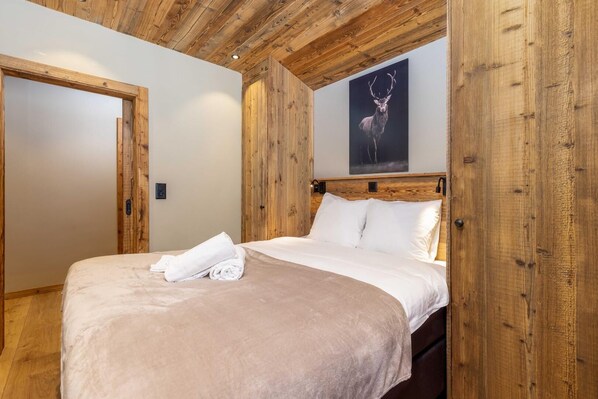 Un dormitorio con techo de madera, una cama con ropa blanca y un cuadro de un ciervo en la pared.