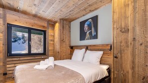 Une chambre dans une cabane en bois, avec un grand lit, une fenêtre donnant sur un paysage enneigé et un tableau accroché au mur.