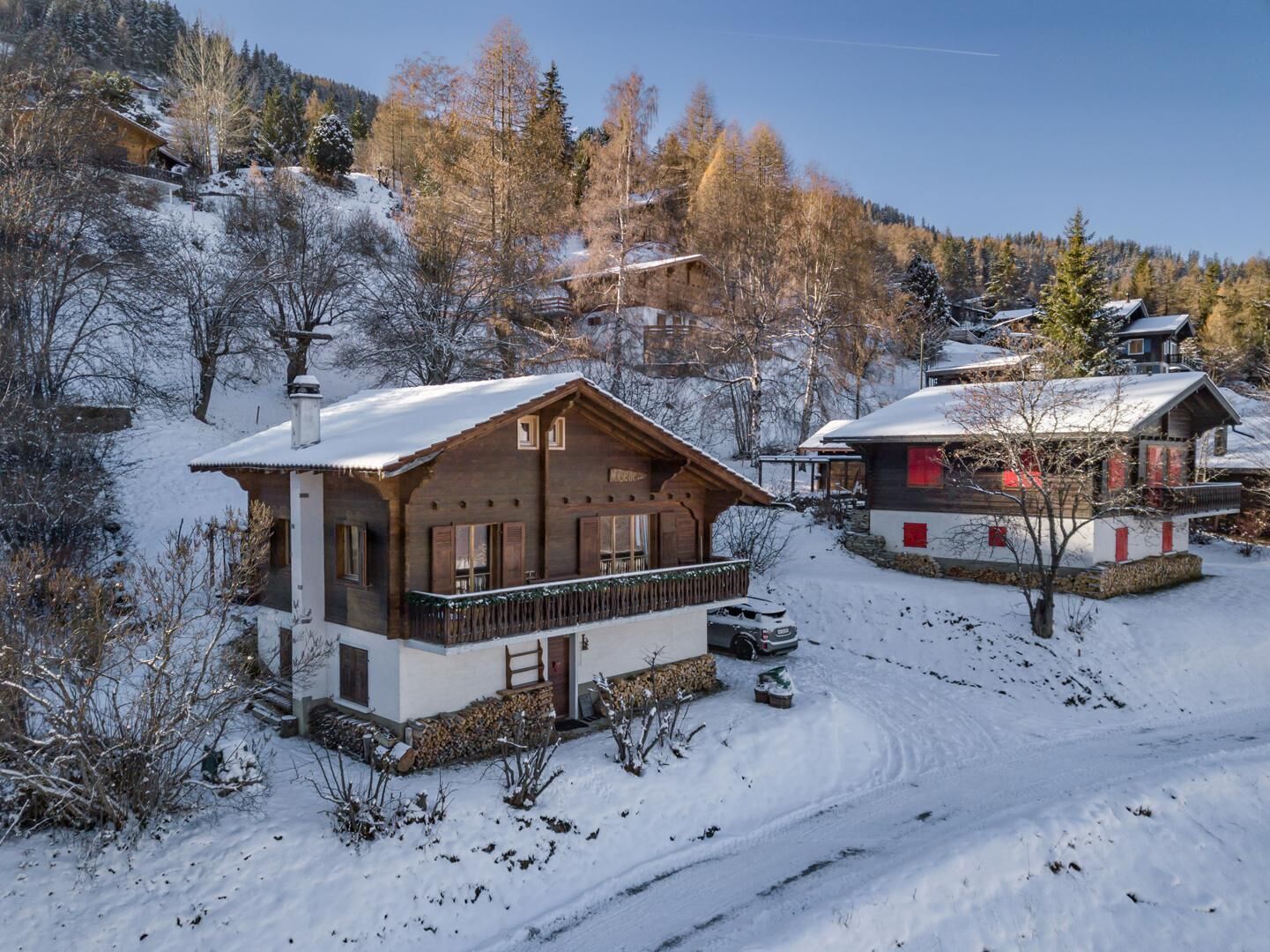 A wooden chalet with a balcony, surrounded by snow-covered trees and a clear sky.