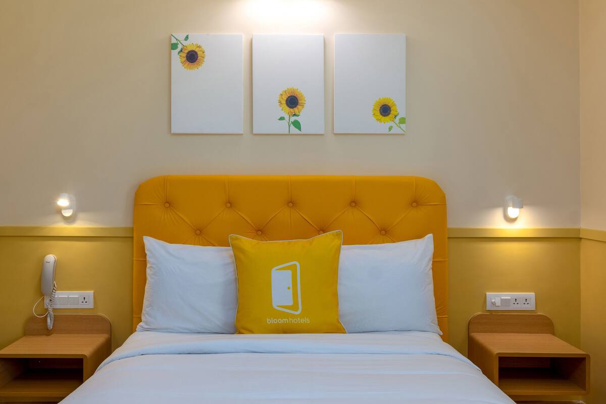 A hotel room with a yellow headboard, white bedding, and three sunflower paintings on the wall.