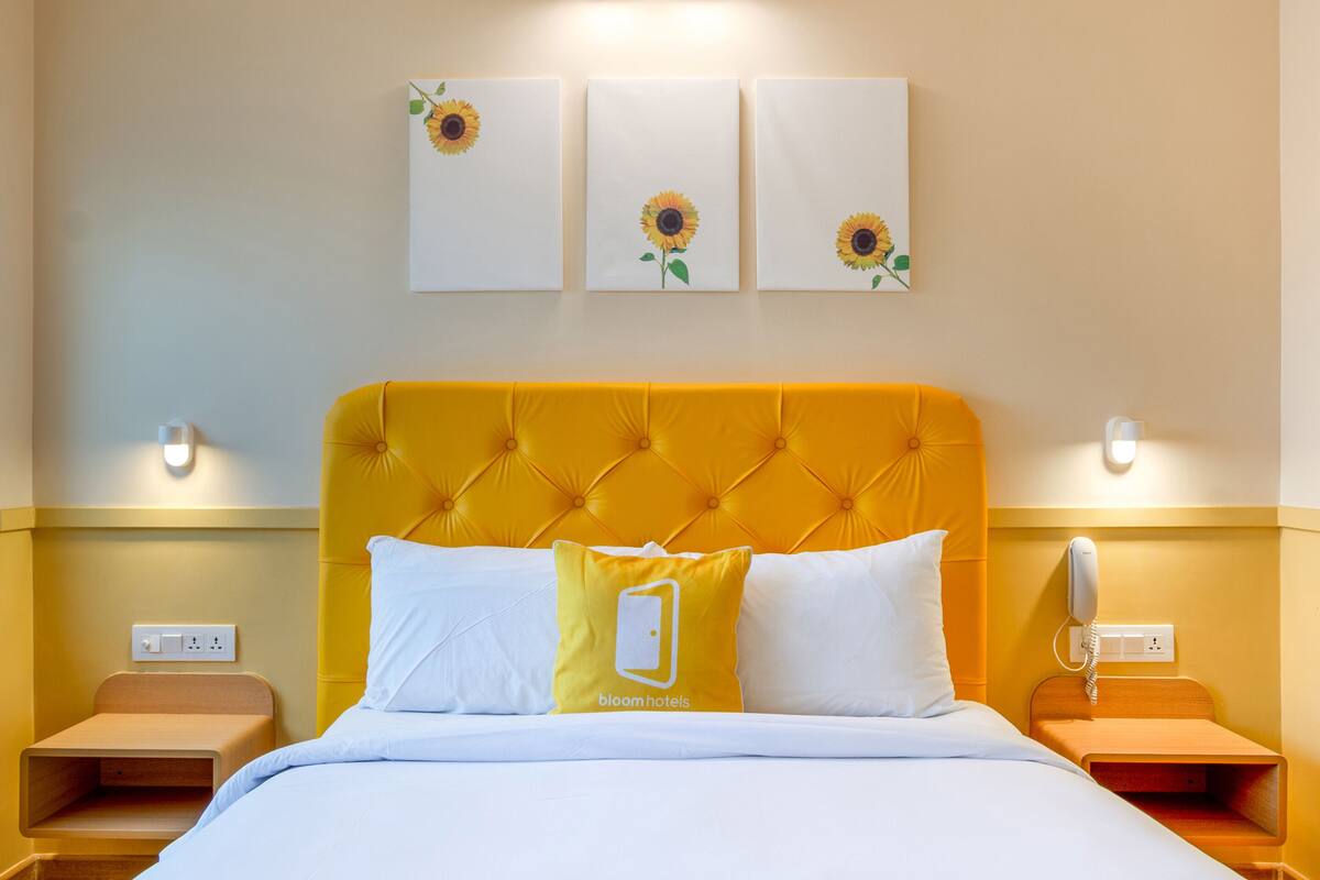 A hotel room with a yellow tufted headboard, white bedding, and three sunflowers on the wall.
