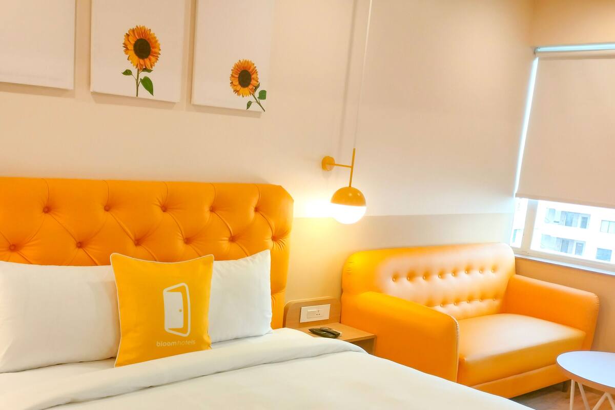 A hotel room with a large bed, a tufted orange headboard, a white and yellow sofa, and a small table.