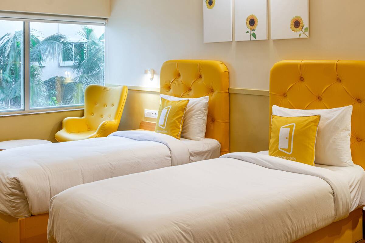 A hotel room with two beds, yellow headboards, white bedding, and a window with a view of palm trees.