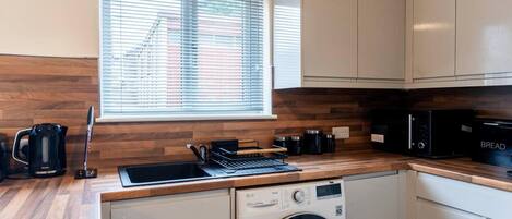 A compact kitchen with a washing machine, a coffee maker, and a microwave.