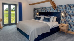 Ett sovrum med en stor säng, ett träbord som används som nattduksbord och utsikt över ett grönskande landskap genom en skjutdörr.