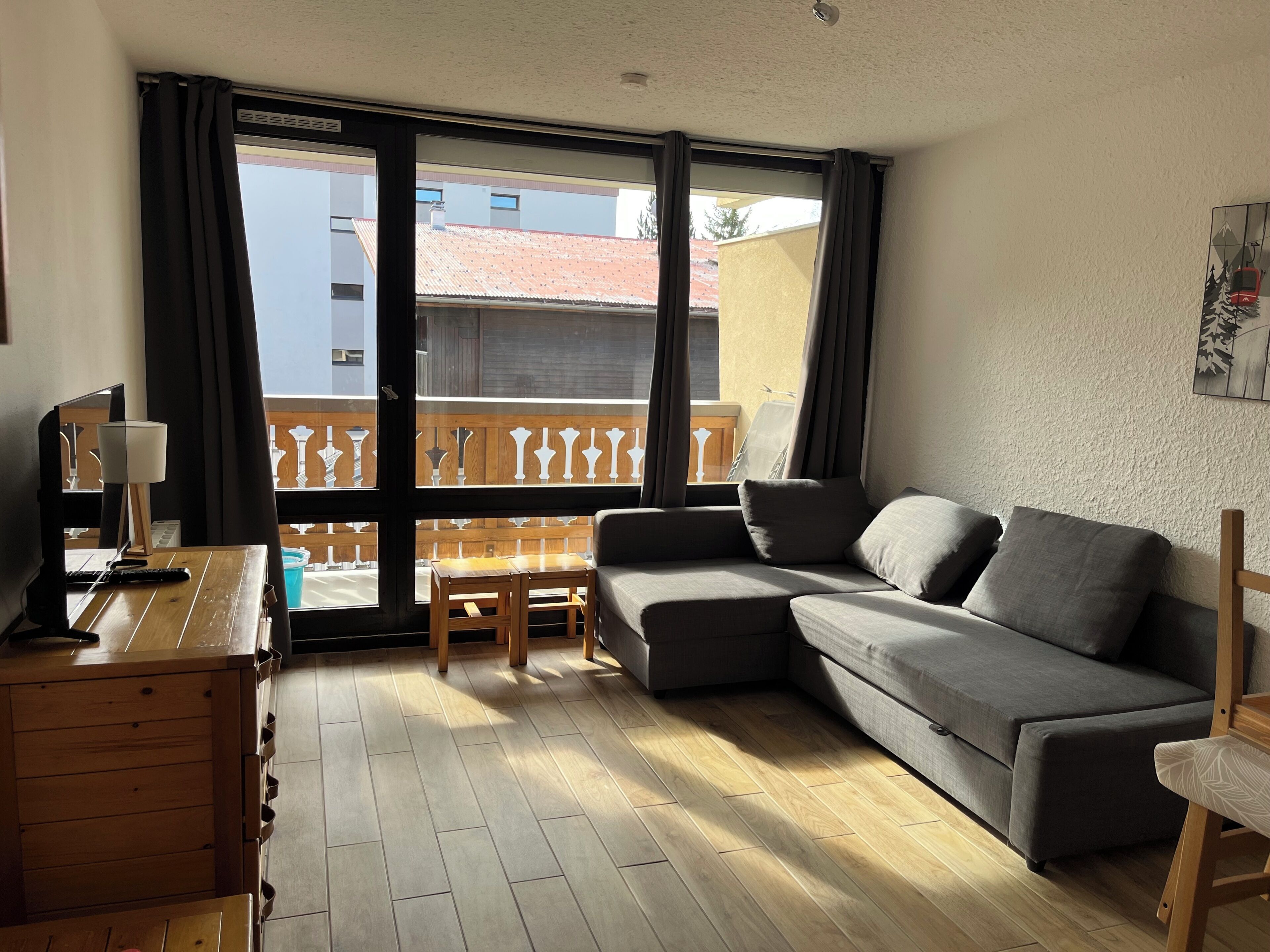 Ein Wohnzimmer mit einer Couch, einem Holztisch, einer Lampe und Blick durch ein großes Fenster.