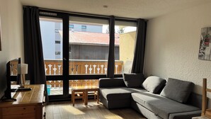 A living room with a sofa, a wooden table, a lamp, and a view through a large window.