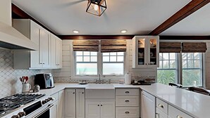 A kitchen with white cabinets, a gas stove, a window with blinds, and a view of the outdoors. - Ocean & Creekfront: Selah mid Island, Porches, Decks, Dock (Pawleys Island)